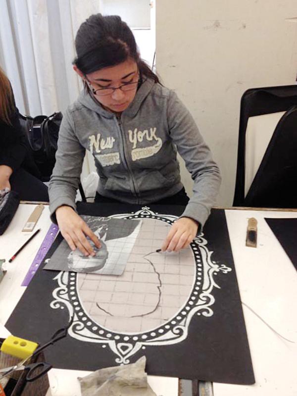 Katherine Caballos using charcoal on gray toned paper and white pencil on black paper. She gridded the paper to help her better accurately draw the portrait. 